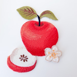 Könnte beinhalten: Stick-on-Patch-Set mit Stickerei, bestehend aus einem roten Apfel mit grünem Blatt, einer roten Apfelscheibe und einer weißen Blüte mit gelber Mitte.