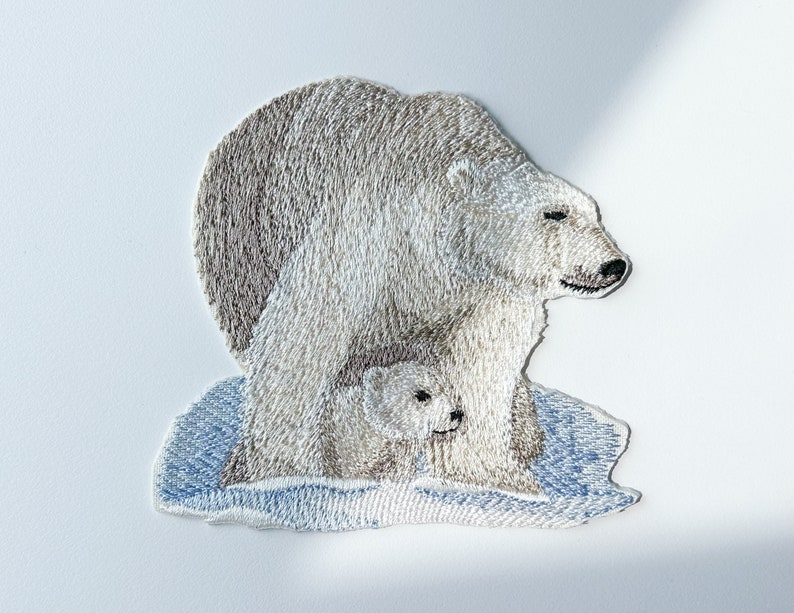 May include: Embroidered patch of a polar bear and cub standing on a blue and white icy surface.