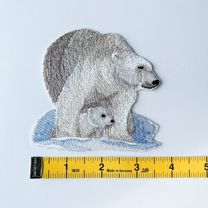 May include: Embroidered patch of a white polar bear with a cub on a blue ice floe. The patch is approximately 2 inches wide.
