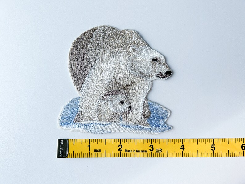 May include: Embroidered patch of a white polar bear with a cub on a blue ice floe. The patch is approximately 2 inches wide.
