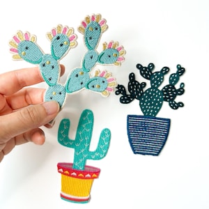May include: Three embroidered cactus patches. One is a light blue prickly pear shape with pink and gold accents. Another is a dark green cactus in a blue striped pot. The third is a light green saguaro-style cactus in a yellow and red pot.
