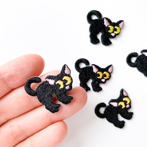 May include: Five black embroidered iron-on patches of cartoon cats with yellow eyes and pink cheeks.