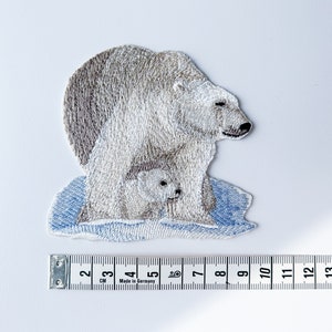 May include: Embroidered patch of a white polar bear with a cub on a blue ice floe. The patch is approximately 7 cm wide.
