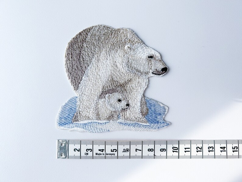 May include: Embroidered patch of a white polar bear with a cub on a blue ice floe. The patch is approximately 7 cm wide.