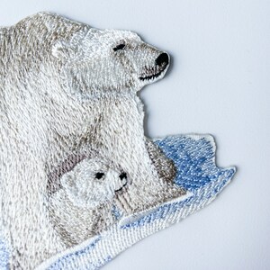 May include: Embroidered patch of a white polar bear with a cub on a blue and white ice floe.