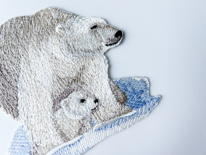 May include: Embroidered patch of a white polar bear with a cub on a blue and white ice floe.