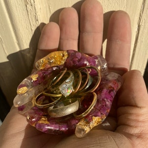 May include: A purple and gold resin ring holder shaped like a hand, with multiple rings inside, including a diamond ring.