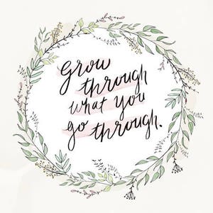 May include: A watercolour print with the handwritten phrase "grow through what you go through" in black script. The text is encircled by a delicate wreath of green and lavender leaves and sprigs, set against a soft, off-white background.
