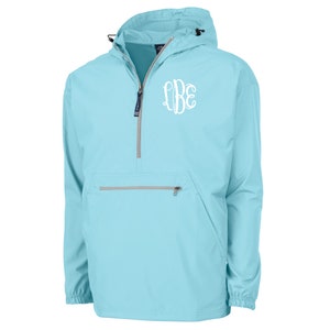 May include: A light blue anorak jacket with a hood and a quarter-zip closure. The jacket features a white monogram on the chest and a front pocket with a zipper. The jacket has a drawstring at the hood and the bottom hem.