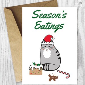 May include: A Christmas card featuring a gray cat wearing a Santa hat and a white beard. The cat is sitting next to a gingerbread man, a candy cane, and a decorated cake. The text on the card reads "Season's Eatings".