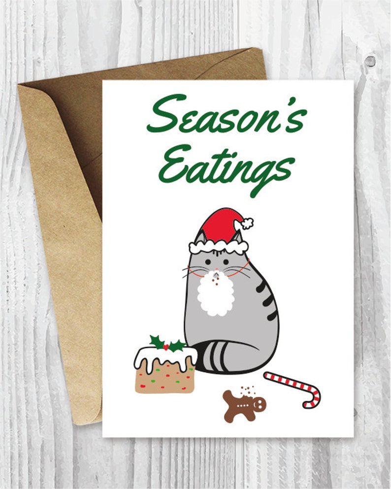 May include: A Christmas card featuring a gray cat wearing a Santa hat and a white beard. The cat is sitting next to a gingerbread man, a candy cane, and a decorated cake. The text on the card reads "Season's Eatings".