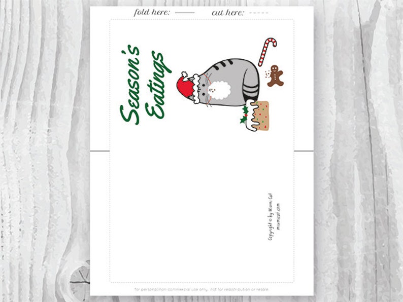 May include: A printable Christmas card featuring a gray cat wearing a Santa hat and holding a gingerbread house. The text "Season's Eatings" is written in green cursive on the card.