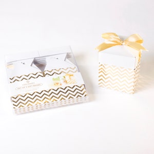 May include: White gift boxes with gold chevron pattern. One box is tied with a gold ribbon. A set of five boxes is in a clear plastic container. The text on the set of boxes reads "SET OF 5 GIFT BOXES".