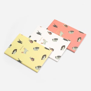 May include: Three notebooks with cat illustrations in yellow, white, and coral. Each notebook has a different color background and features a repeating pattern of various cat poses. The word "NOTES" is printed on each cover.