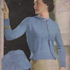 May include: A blue knitted cardigan with a matching blue knitted top. The cardigan has a V-neck and buttons down the front. The top has a round neckline. The model is wearing a light beige skirt. The image includes the text "Marriners Heritage 3-ply 32.34.36.38 & 40" bust" and "Jackson Prop. Wm. Jackson Market Street. Kirkey, Stepney Art Needlework Wools, Babywear, etc."