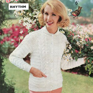 May include: A white knitted cardigan with a cable knit pattern and a pocket on the front. The cardigan is buttoned up and the model is wearing a pink skirt. The image is from a vintage knitting pattern book.