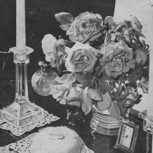 Puede incluir: Una fotografía en blanco y negro de un encaje de ganchillo con un frasco de vidrio en el centro. El encaje está sobre una mesa con un candelero, un jarrón de rosas y un reloj pequeño. El texto "BESTWAY 1942 3d. TWO SETS OF MATS For a DUCHESSE SET or for LUNCHEON MATS W.B. Sobritto Crochet (Art Silk)" está impreso en un cartel sobre la mesa.