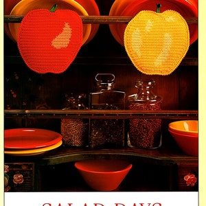 Puede incluir: Dos agarraderas de olla de ganchillo con forma de manzana, una roja y otra amarilla, colgadas de una estantería de madera con otros artículos de cocina. "SALAD DAYS" está escrito en letras rojas debajo de la imagen. Dale un toque alegre a tu cocina con estas agarraderas de olla originales. Hechas con algodón de 4 hebras, son fáciles de hacer y sus colores vivos alegrarán los días más grises.