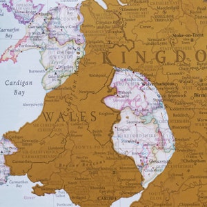 May include: A gold-toned map of the United Kingdom with a focus on Wales. The map highlights major cities, towns, and geographical features. The map is framed with a brown border.