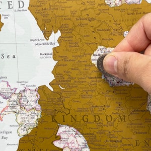 May include: A gold-colored map of the United Kingdom with push pins marking locations. The map is on a white background and includes the names of cities and towns throughout the country.