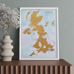 May include: A white framed scratch-off map of the United Kingdom with gold foil covering the map. The map is titled "Scratch U.K."