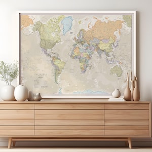 May include: A framed world map with a beige background and colorful country borders. The map is hanging on a white wall above a light brown wooden dresser.