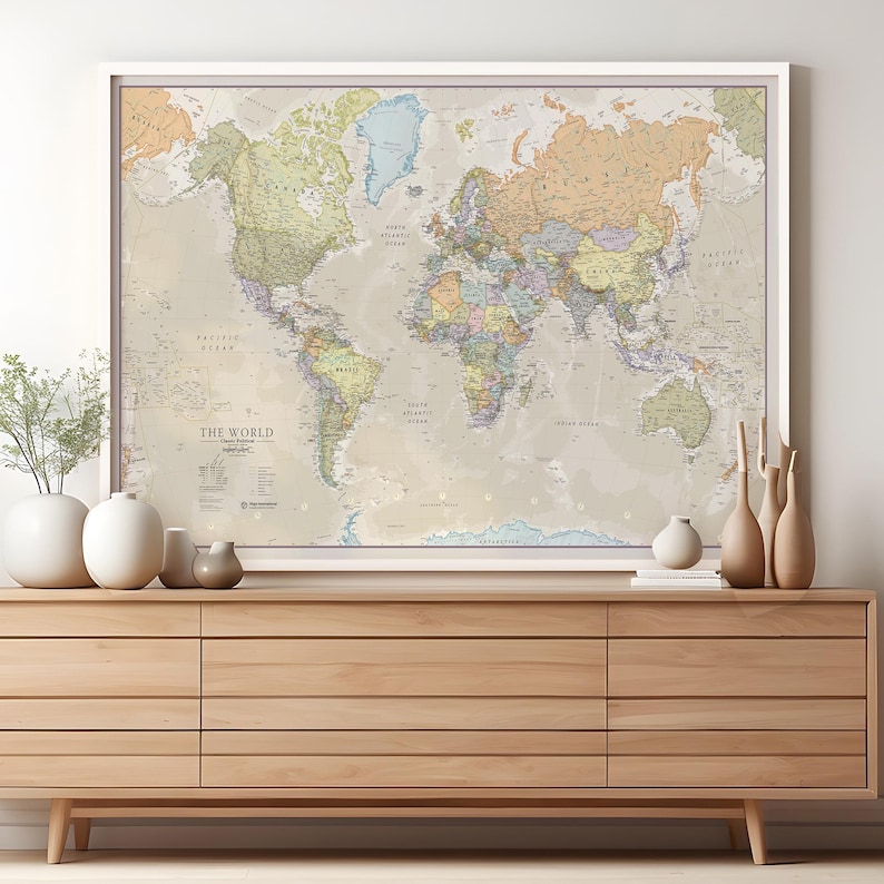 May include: A framed world map with a beige background and colorful country borders. The map is hanging on a white wall above a light brown wooden dresser.