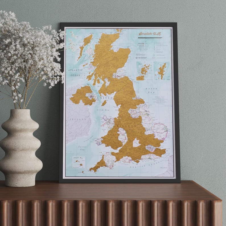 May include: A framed scratch-off map of the United Kingdom with a gold foil finish. The map is in a black frame and shows the different regions of the UK. The map is on a wooden surface.