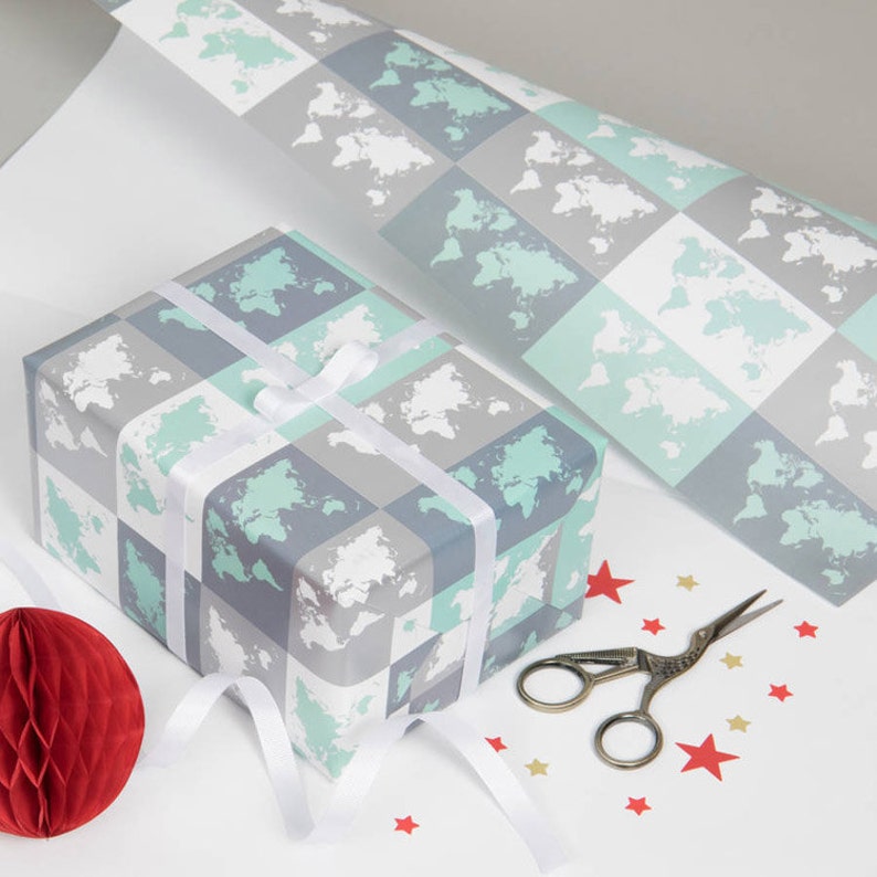 May include: A gift wrapped in white wrapping paper with a pattern of grey and light blue squares with a world map design. The gift is tied with a white ribbon and there are red stars scattered around the gift.