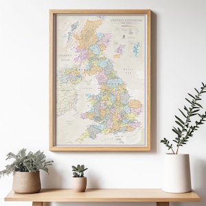 May include: A framed map of the United Kingdom in a vintage style. The map is in a light brown frame and shows the different counties of England, Scotland, and Wales. The map is on a white wall with a plant in a white pot on a wooden shelf.