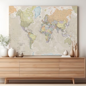 May include: A large world map canvas print in a vintage style, showing continents and countries in muted tones. The map is displayed above a wooden sideboard with decorative vases and plants.