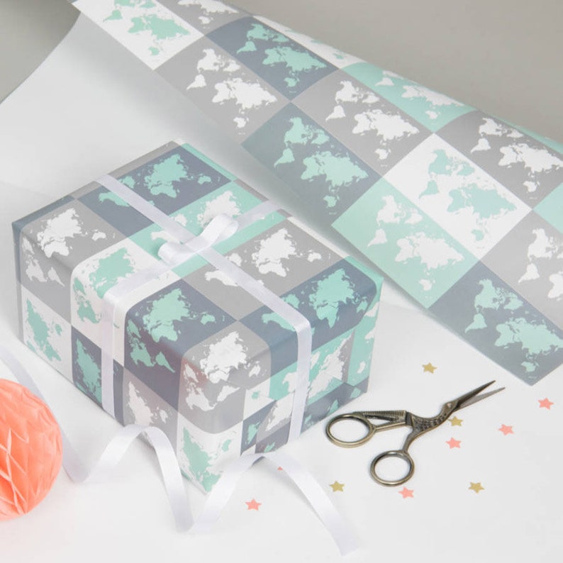 May include: A gift wrapped in blue and green wrapping paper with a world map pattern. The paper is wrapped around a box with a white ribbon. There are gold stars scattered on the surface.
