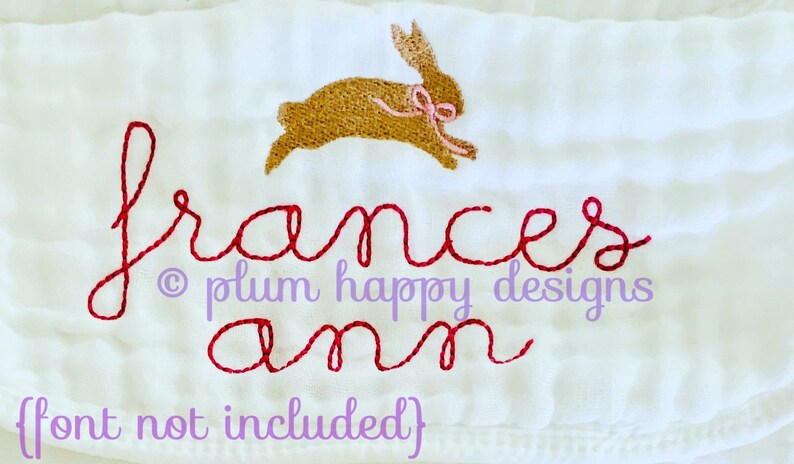 May include: A white embroidered baby blanket with the name "Frances Ann" in red cursive script and a brown bunny with a pink bow above the name. The text "&copy; plum happy designs" is below the name.