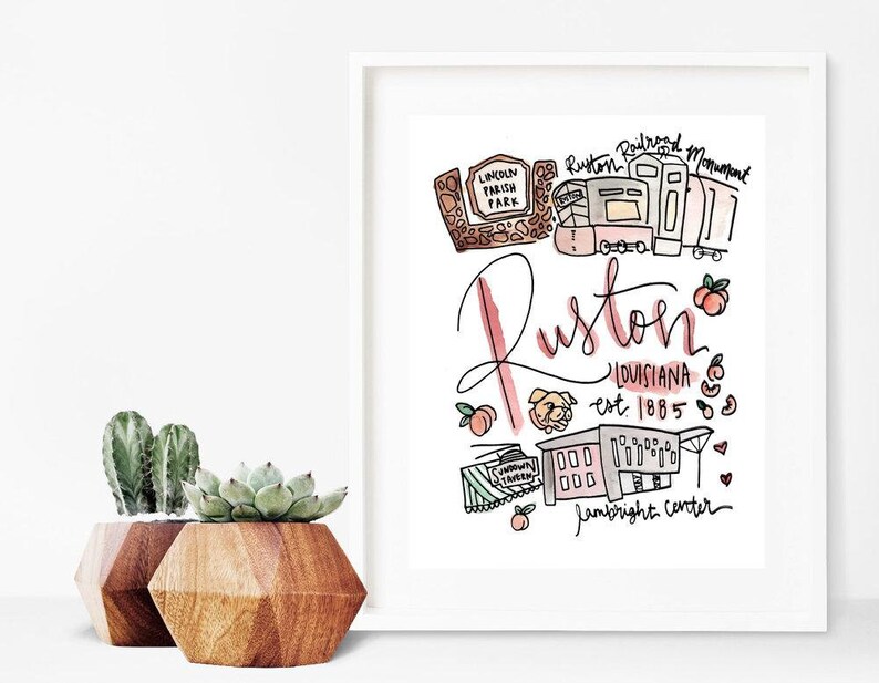 May include: A framed watercolor print featuring the word "Ruston" in cursive, with illustrations of local landmarks and the text "Louisiana est. 1885." The print includes images of peaches, a dog, and a train.