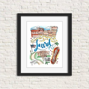 Puede incluir: Una impresión en acuarela enmarcada con una colorida ilustración de Laurel, MS. La obra de arte incluye el nombre de la ciudad en cursiva, una bandera estadounidense ondeando y lugares emblemáticos locales. La impresión está en un marco negro y cuelga de una pared de ladrillo blanco.
