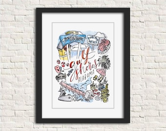 May include: A framed watercolor print featuring a colorful map of Gulf Shores, Alabama. The artwork includes illustrations of local landmarks, the text "The Hangout," and "Shrimp Basket." The print is in a black frame and is displayed against a white brick wall.