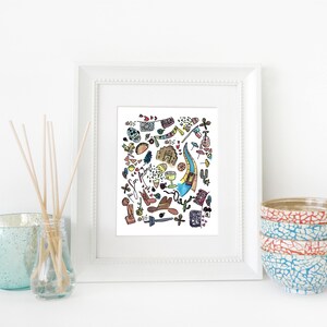May include: A framed art print with a white border, featuring a colorful doodle-style illustration of various objects. The print is displayed on a white surface, alongside a stack of decorative bowls and a glass diffuser with reeds.