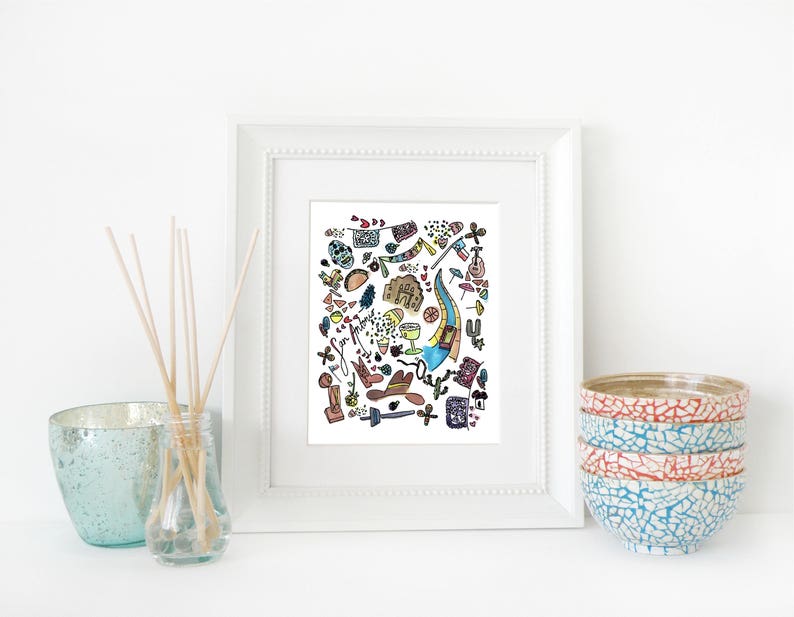 May include: A framed art print with a white border, featuring a colorful doodle-style illustration of various objects. The print is displayed on a white surface, alongside a stack of decorative bowls and a glass diffuser with reeds.