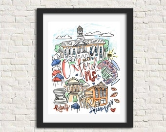 Op de afbeelding: Een ingelijste kunstdruk met een kleurrijke illustratie van bezienswaardigheden in Oxford, MS. Het kunstwerk bevat de tekst "Oxford MS", "Rebels" en "Square Books", met afbeeldingen van gebouwen en een stadion. De print zit in een zwarte lijst.