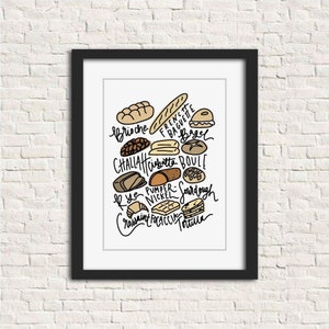 May include: A framed print featuring various types of bread, including brioche, baguette, and bagel. The names of the breads are handwritten in black ink, with illustrations of each bread type. The print is displayed against a white brick wall.