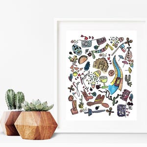 May include: A framed watercolor print featuring colorful illustrations of San Antonio landmarks and cultural symbols. The artwork includes a skull, guitar, river, and the text "San Antonio". Two wooden geometric planters with succulents are in the foreground.