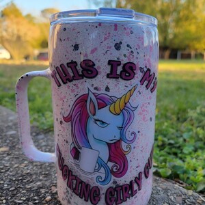 May include: White stainless steel travel mug with a pink, white, and blue unicorn graphic. The mug has a pink lid and a handle. The text "This is my f***ing girly cup" is printed on the mug.