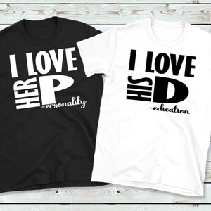 May include: Two matching t-shirts, one black and one white. The black shirt says "I LOVE HER P - personality" in white block letters. The white shirt says "I LOVE HIS D - education" in black block letters. Both shirts are crew neck.