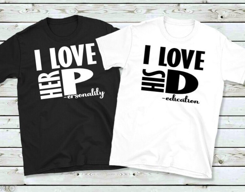 May include: Two matching t-shirts, one black and one white. The black shirt says "I LOVE HER P - personality" in white block letters. The white shirt says "I LOVE HIS D - education" in black block letters. Both shirts are crew neck.
