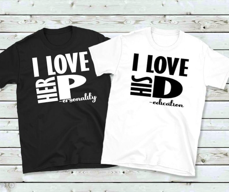 May include: Two matching t-shirts, one black and one white. The black shirt says "I LOVE HER P - personality" in white block letters. The white shirt says "I LOVE HIS D - education" in black block letters.