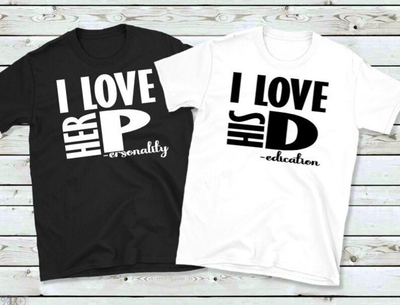 May include: Two t-shirts, one black and one white, with bold black text. The black shirt reads "I LOVE HER P - personality" and the white shirt says "I LOVE HIS D - education". Both shirts have a crew neck.