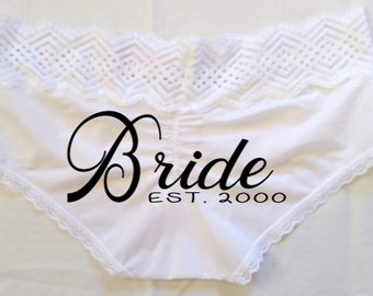 May include: White underwear with a lace trim and the word "Bride" in a black script font. The text "EST. 2000" is below the word "Bride". The underwear has a decorative lace trim.