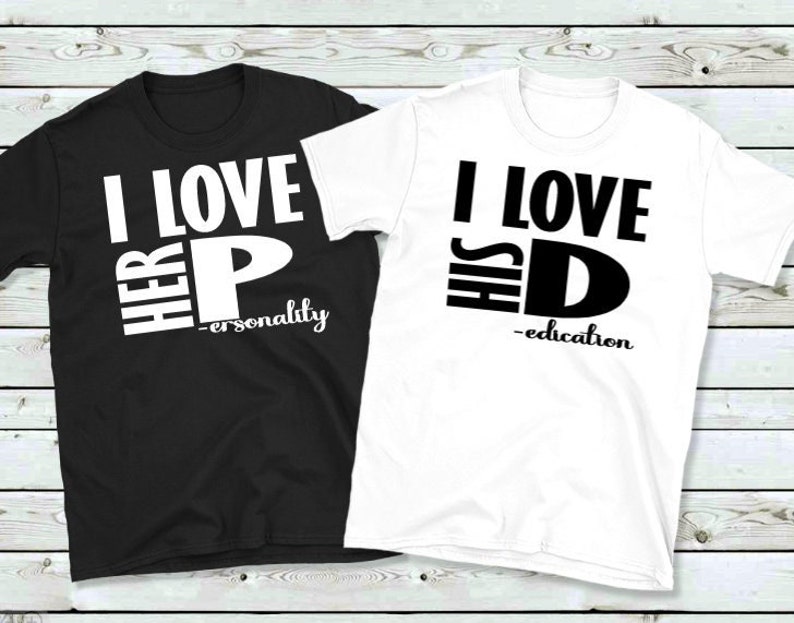May include: Two matching t-shirts, one black and one white. The black shirt says "I LOVE HER P - personality" in white block letters. The white shirt says "I LOVE HIS D - education" in black block letters. Both shirts are short-sleeved.