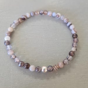 May include: A bracelet made of small, round, grey, white, and brown agate beads with a silver bead accent.