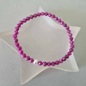 May include: A pink gemstone bracelet with a silver bead accent. The bracelet is made of small, faceted beads and is strung on a thin, elastic cord.